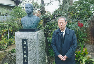 必勝氏の像の前で